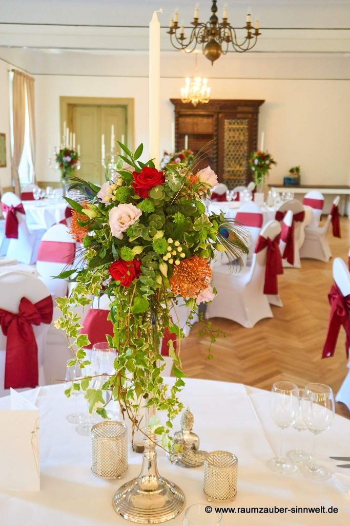 Tischdekoration aus roten Rosen, Nadelkissen, Eustoma, Hypericum und Pfauenfedern