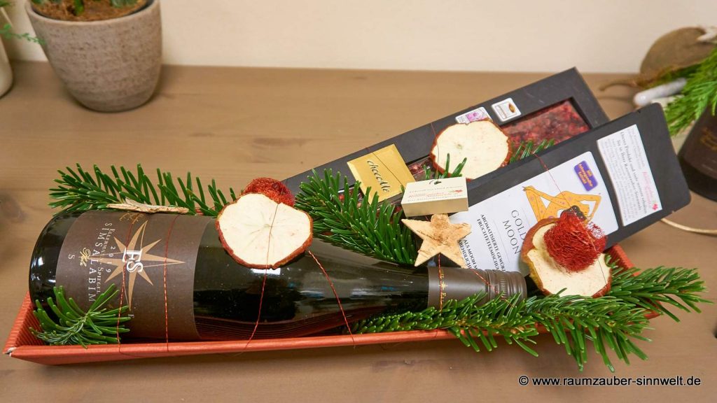 Weinflasche von ELLERMANN-SPIEGEL, Gute-Nacht-Tee von Wollenhaupt und Schokolade chocoMe weihnachtlich dekoriert.