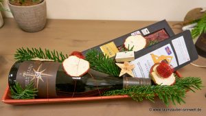 Weinflasche von ELLERMANN-SPIEGEL, Gute-Nacht-Tee von Wollenhaupt und Schokolade chocoMe weihnachtlich dekoriert.