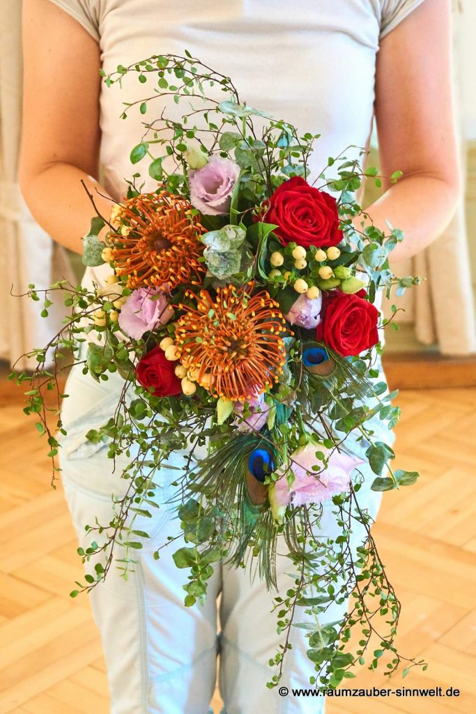 Extravaganter Brautstrauß in Wasserfallform aus Nadelkissen, roten Rosen, Eustoma, Hypericum, Eucalyptus und Pfauenfedern.