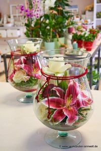 Tischgestecke im Glas mit Rosen und Lilien.