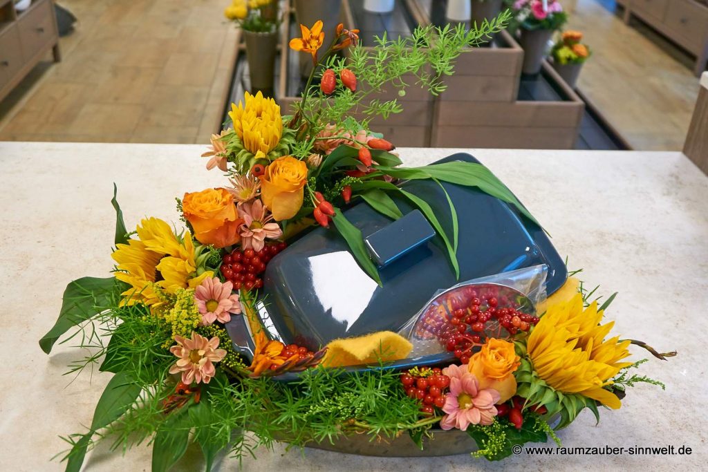 Thermomix-Bräter als Präsent floral verpackt mit Frischblumengesteck aus Rosen, Sonnenblumen und Hagebutten.