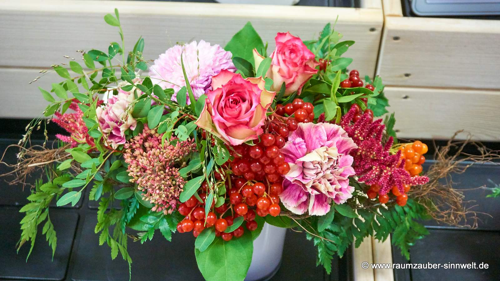 Querstrauß aus Rosen, Nelken, Sedum und Beeren.