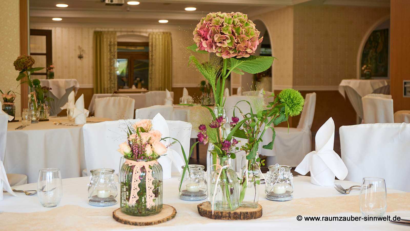 Tischdekoration aus Hortensie, Astrantie, Bartnelke, Rosen und Gräsern in Gläsern auf Baumscheibe