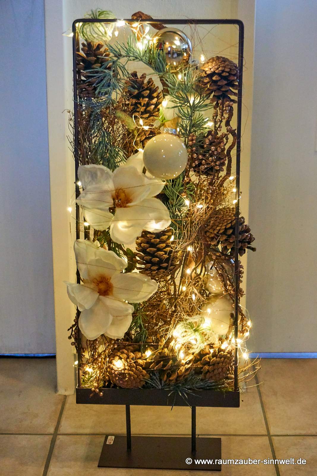 Weihnachtsdekoration aus Naturmaterialien, Seidenblüten und Kugeln im Metallständer mit LED-Lichterkette