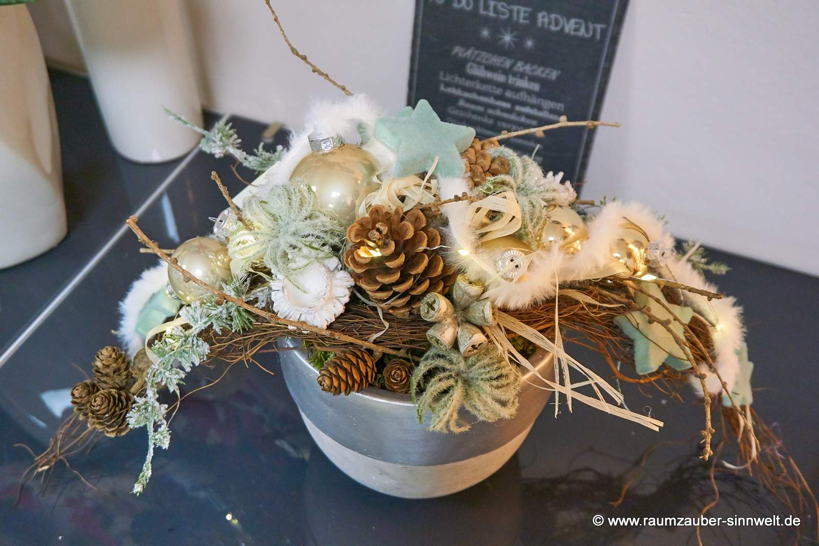 Weihnachtsdekorationen aus Naturmaterialien, Seidenblüten und Kugeln im Keramikgefäß mit LED-Lichterkette