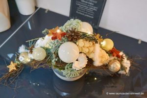 Weihnachtsdekorationen aus Naturmaterialien, Seidenblüten und Kugeln im Keramikgefäß mit LED-Lichterkette