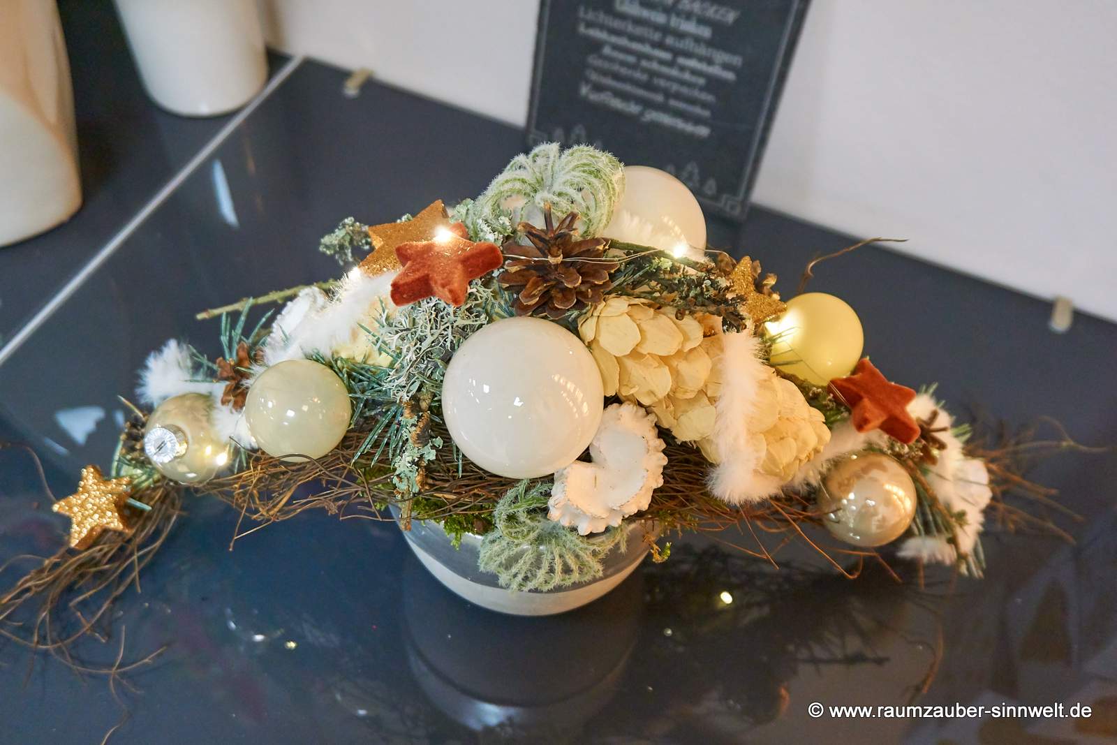 Weihnachtsdekorationen aus Naturmaterialien, Seidenblüten und Kugeln im Keramikgefäß mit LED-Lichterkette