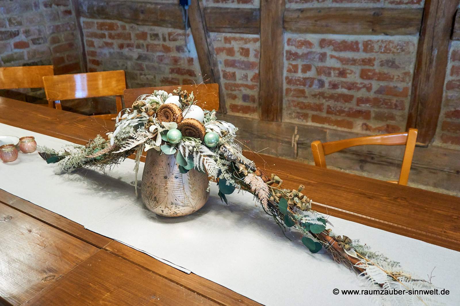 Winterliche Tischdekoration aus Naturmaterialien und Kugeln im Glasgefäß.