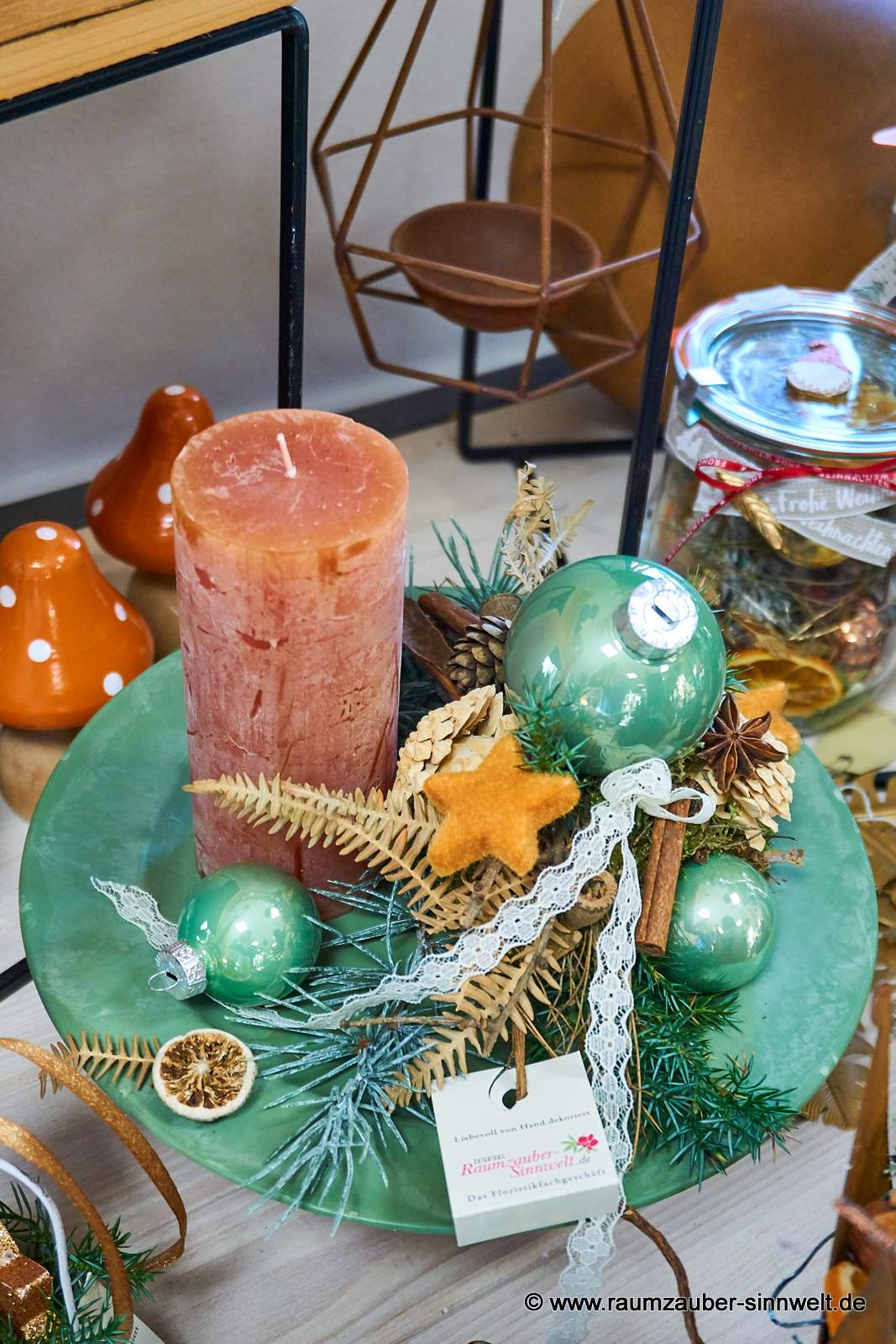 Handgefertigtes Adventsgesteck aus Naturmaterialien und Kugeln auf Keramikteller mit Kerze weihnachtlich dekoriert.