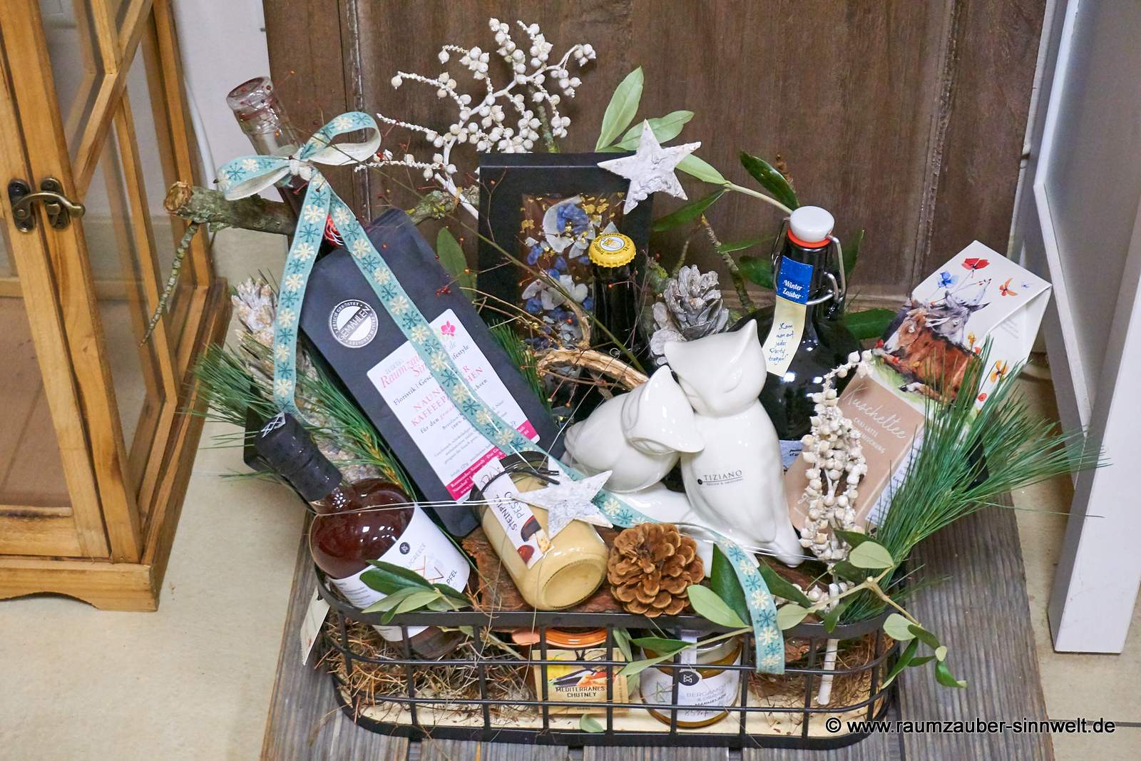 Großer Präsentkorb gefüllt mit Produkten kleiner Feinkostmanufakturen: vollmundiger Balsamico aus natürlichen, sonnenverwöhnten Zutaten und Konfitüre aus Kreta, naturbelassenem Kräutertee vom Grätzverlag, Kaffee aus sächsischer Kaffeemanufaktur, Schokolade von chocoMe, Pesto, Chutney und Eulenpaar Cicero von Tiziano weihnachtlich dekoriert.