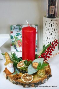 Handgefertigtes Adventsgesteck aus Naturmaterialien auf Holzscheibe mit Kerze und Wichtel weihnachtlich dekoriert.