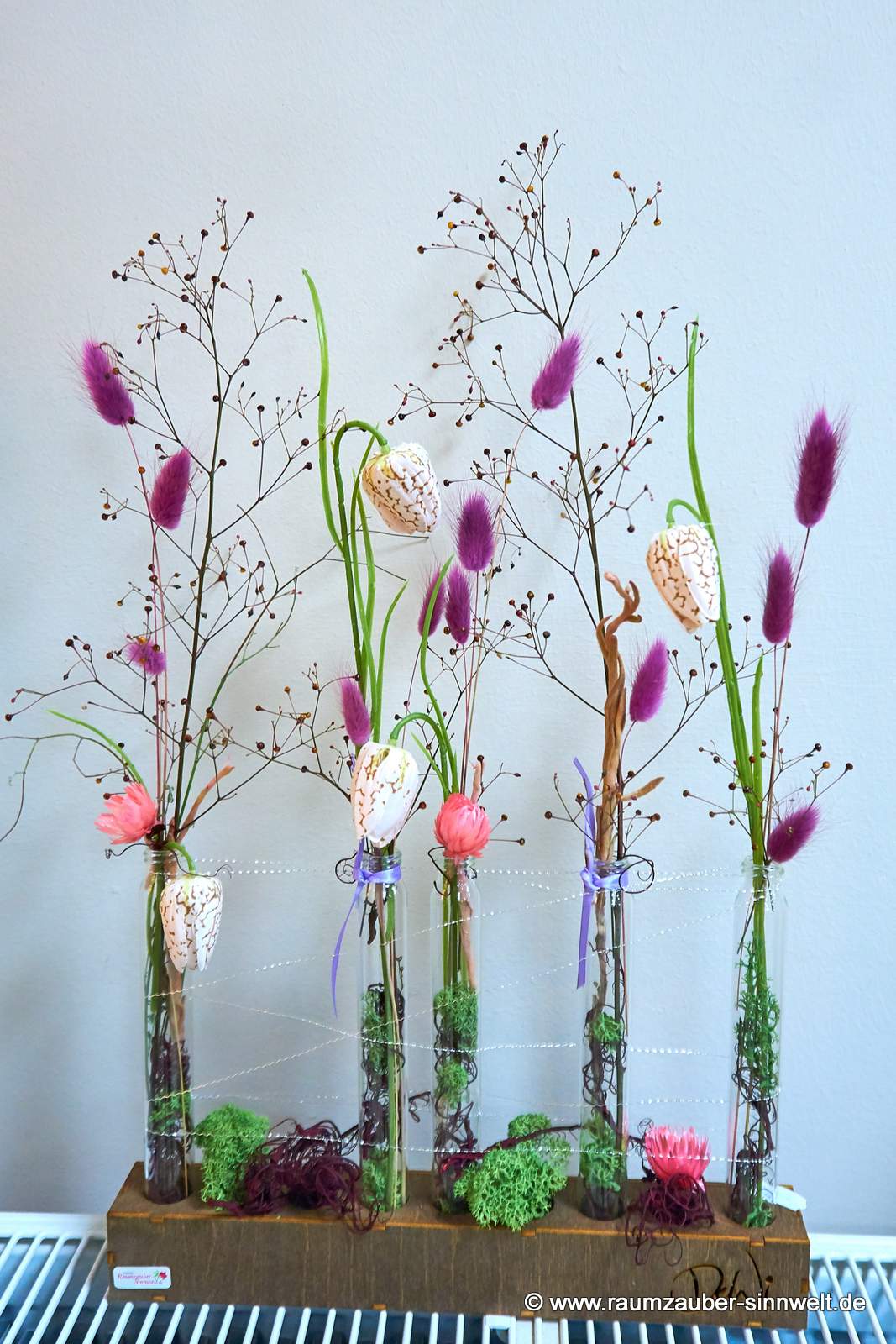 Trockendekoration aus Gräsern und Seidenblüten in Glasröhrchen in Holzständer