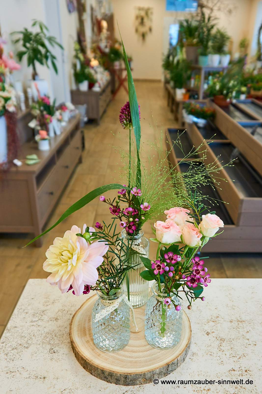 Tischdekoration aus drei kleinen Vasen gefüllt mit Rosen, Waxflower, Panicum, und Dahlien auf Baumscheibe.