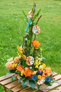 Geldpräsent mit Quietscheentchen und Gitarre in Frischblumengesteck aus Lilien, Rosen, Santini und Distel