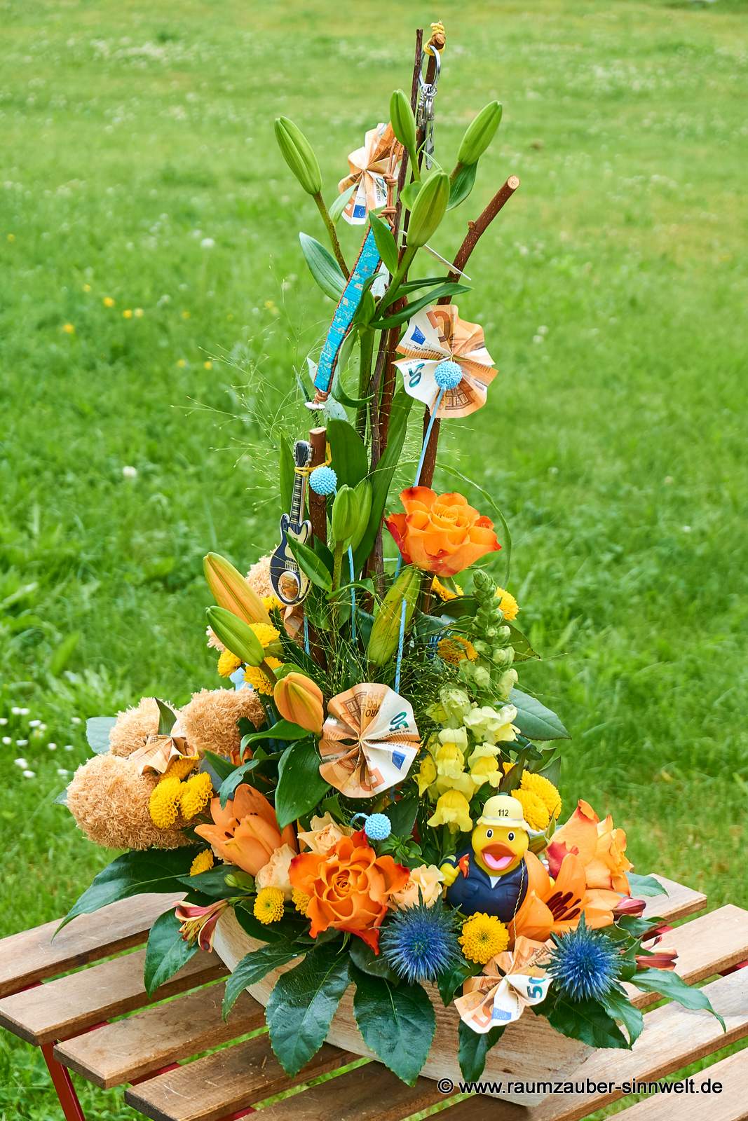 Geldpräsent mit Quietscheentchen in Frischblumengesteck aus Lilien, Rosen, Santini und Distel