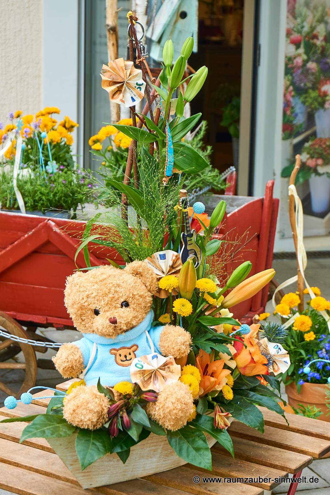 Geldpräsent mit Lieblingsteddy in Frischblumengesteck aus Lilien, Rosen, Santini und Distel