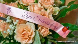 Rundstrauß aus Rosen und Schleierkraut mit Stiften und Malbuch vom Grätz-Verlag zum Schulanfang.